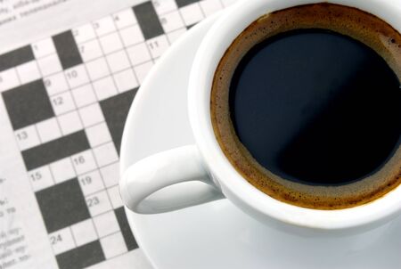white cup of coffee and a newspaper with a crossword puzzle on the tableの写真素材