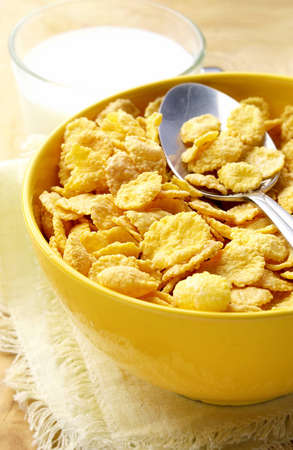 milk in a glass cup and corn flakes in a yellow bowl