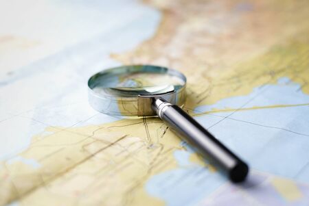 Low angle view of a map with a small round chrome metal magnifying glass lying on top facing away from the cameraの写真素材
