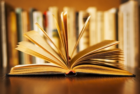 Hardcover book lying open on its cover with the pages fanned above it and a row of books on a bookshelf visible behind, shallow dofの写真素材