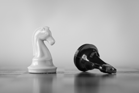 Two knights in a game of chess with the vanquished black chess piece lying on its side and the white knight standing upright signifying successの写真素材