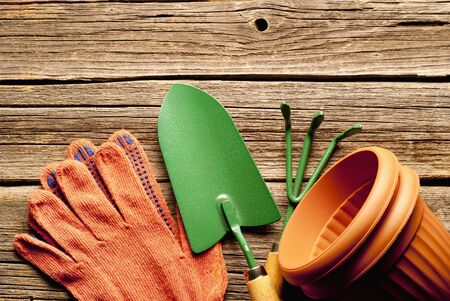 Conceptual image of gardening equipment consisting of gloves, clay flowerpots and a small trowel and fork lying on rustic wooden boards with copyspace aboveの写真素材