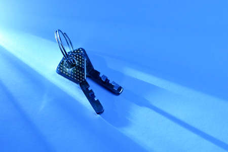 Two silver metallic keys with a textured surface lying in a beam of light shining across a blue...