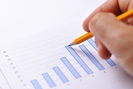 Close up view of a male hand holding a pencil analysing a fluctuating bar graph showing business performanceの写真素材