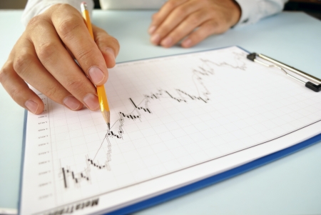 Close up view of the hand of a man analysing an upward trending graph attached to a clipboard...