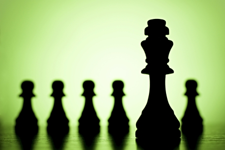 King and pawns - chess pieces silhouetted against a green background with copyspace conceptual of leadership and individualityの写真素材