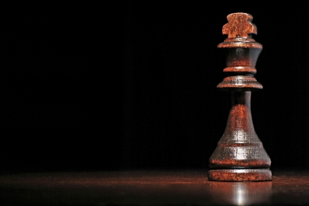 Low angle view of a dark wood king chess piece on a reflective wooden surface against a dark background with copyspaceの写真素材