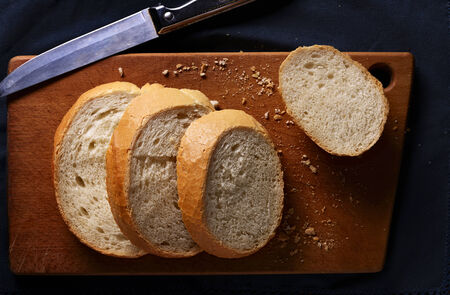 Sliced freshly baked golden crisp crusty baguette lying on a wooden cutting board, close up overhead...