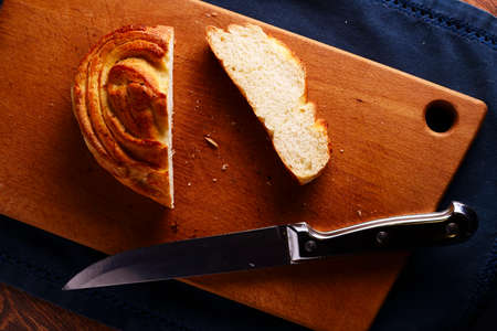 Overhead view of a cut bun with the slice lying alongside on a wooden breadboard with a sharp kitchen knife on a black の写真素材