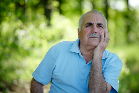 Elderly grey-haired retired man with a moustache sitting outdoors in a lush green park smiling at the cameraの写真素材