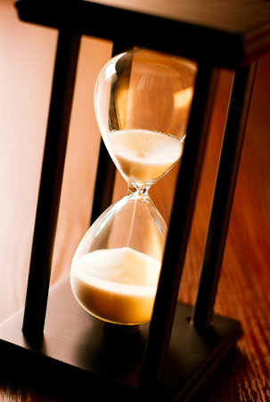 Close up of a wooden hourglass with running sand and glass bulb measuring the passing time to a deadline or end pointの写真素材