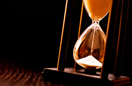 Newly turned hourglass with running sand measuring the passing time to a deadline or expiry of a fixed time period, close up on a dark backgroundの写真素材