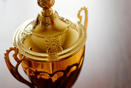 Close up view of ornamental detail on a gold trophy lid with a finial and handles to be awarded to the winner or champion, on grey with copyspaceの写真素材