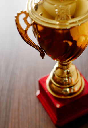 Close up high angle soft focus image of a gold trophy cup with handles and an embossed lid on a red plinthの写真素材