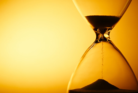 Sand passing through the glass bulbs of an hourglass measuring the passing time as it counts down to a deadline or closure on a yellow background with copyspace Sand passing through the glass bulbs of an hourglass measuring the passing time as it counts down to a deadline or closure on a yellow background with copyspace
