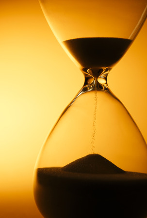 Sand passing through the glass bulbs of an hourglass measuring the passing time as it counts down to a deadline or closure on a yellow background with copyspaceの写真素材