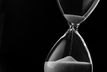 Sand running through the bulbs of an hourglass measuring the passing time in a countdown to a deadline, on a dark background with copyspace Sand running through the bulbs of an hourglass measuring the passing time in a countdown to a deadline, on a dark background with copyspace