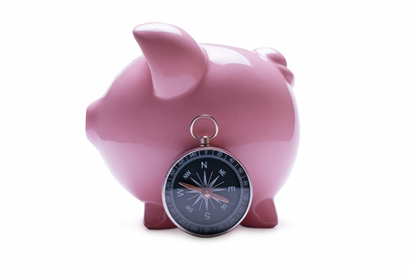 Porcelain pink piggy bank next to a vintage compass, concept of savings and guidance, close-up with shadow on whiteの写真素材