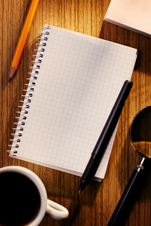 Grid Notebook and Cup of Coffee with Various Stationary Items on Desk as seen from Aboveの写真素材