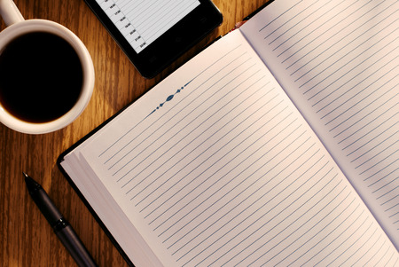 View from above of an open journal or diary with blank lined white pages with copyspace for your text and a mug of black coffee on a wooden deskの写真素材