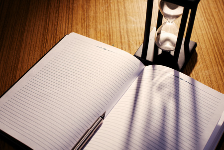 Hourglass Casting Shadow on Lined Notebook with Pen on Desk as seen from Above in Time Concept Image