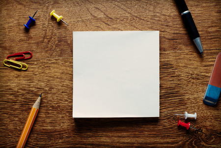 Variety of Office or School Supplies on Top of Wooden Desk with Central Copy Space for Texts. Emphasizing Blank White Paper on the Center.の写真素材