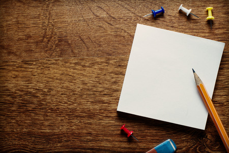 Stack of small square blank white memo pages with a pencil for jotting notes and reminders and thumbtacks to attach to a notice board, overhead view on a wooden deskの写真素材