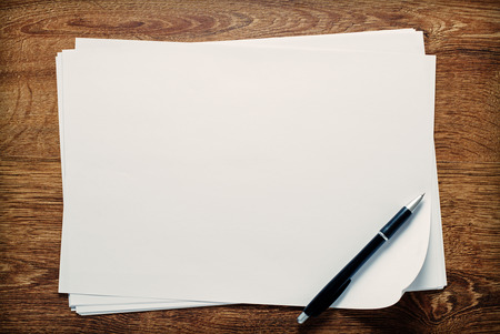 Ballpoint pen lying on sheets of blank white paper with copyspace for your handwriting or text, overhead view on a wooden deskの写真素材