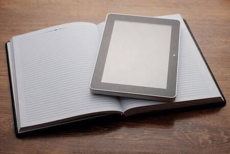 Close up Electronic Tablet Device on Open Clean Notebook Resting on Wooden Table. Emphasizing...