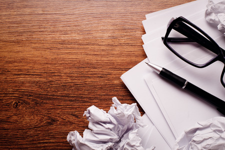 Close up Plain and Crumpled Papers with Pen and Glasses on Top of Brown Wooden Table with Copy Space on Left Side.の写真素材