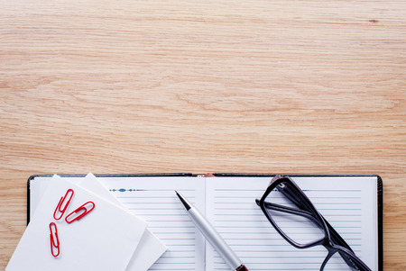 Glasses, pen, clips, notebook lie on light brown desktopの写真素材