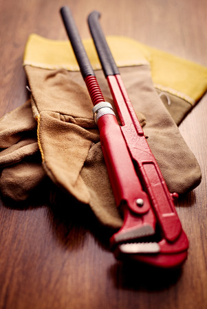 Close up Red Pipe Wrench on Top of a Brown Hand Gloves Above the Wooden Table.の写真素材