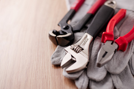 Adjustable wrench, pliers and nail puller on top of the protective gloves on a wooden background