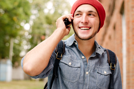 The young man with red cap calls on his cell phone on background with trees and buildingの写真素材