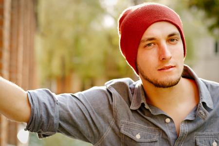 Young modern stylish man with red cap near a wall of the buildingの写真素材