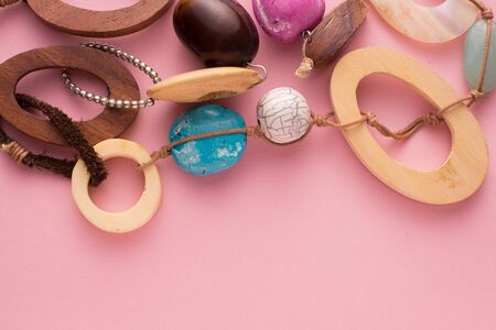 High Angle Close Up Still Life of Handmade Artisan Necklace on Pink Background with Copy Space - Detail of Fashionable Jewellery with Wooden Circles and Colorful Beads and Stones Secured with Leatherの写真素材
