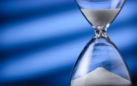 Sand running through an hourglass measuring passing time counting down towards a deadline, close up...