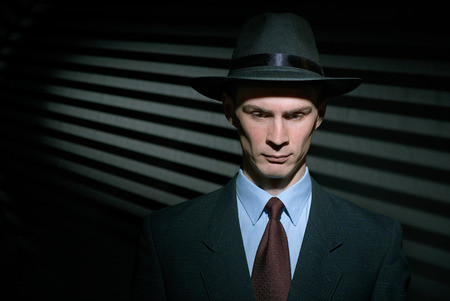 Fashionable young gentleman detective in suit and trilby hat with blinds in background and copy spaceの写真素材