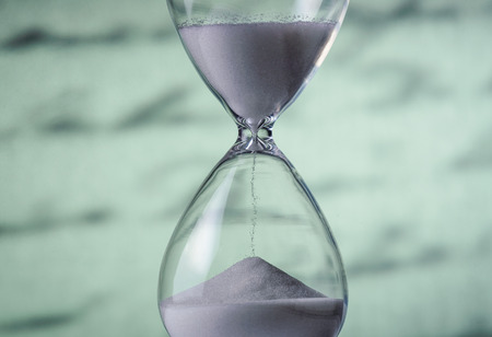 Sand running through an hourglass measuring passing time counting down towards a deadline, close up view of the glass bulbs with a blurred written doent behind and copy spaceの写真素材