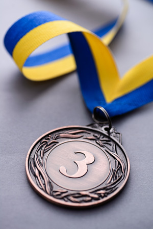 Close-up studio shot of third place bronze medal with striped blue and yellow ribbon on gray backgroundの写真素材