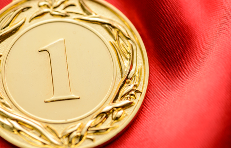 Embossed gold winners medallion for the first place in a competition or championship with a large number 1 in the centre on red fabric with copy spaceの写真素材