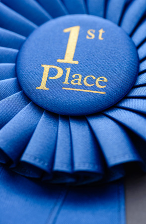Winners blue first place rosette in soft textured fabric and pleated ribbon with a close up view on the central gold textの写真素材