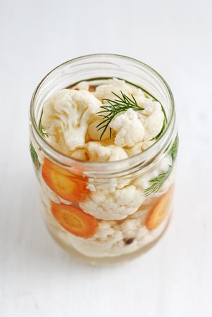 From above shot of open jar of fermented cauliflower with dill and carrot standingon white backgroundの写真素材