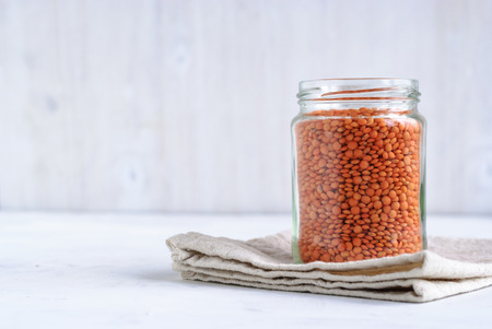 Glass jar filled with orange or red lentils viewed side on standing on a folded kitchen cloth over a white backgroundの写真素材