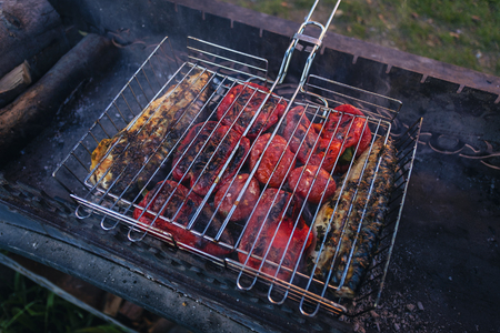 Barbecue with meat and bell pepper preparing on smoking grill, viewed in close-up from high angleの写真素材