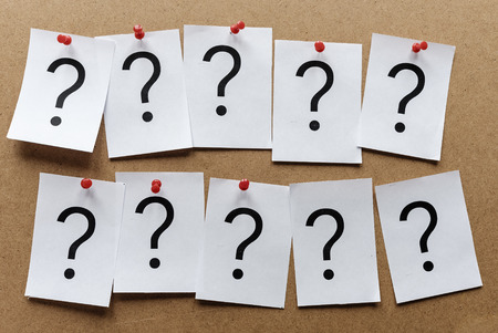 Two rows of question marks printed on individual white cards pinned to a wooden notice board with...