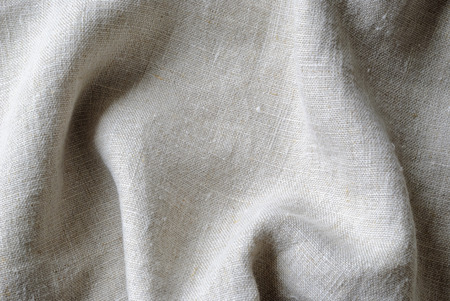 Gathered folded soft woven linen fabric in a neutral natural color in a close up full frame background textureの写真素材