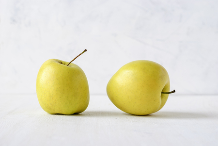 Two ugly misshapen golden fresh apples viewed side by side low angle on whiteの写真素材