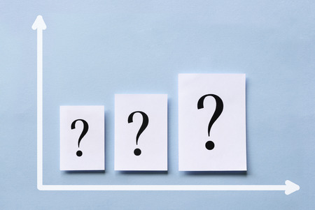 Business chart with a line of question marks printed on white cards arranged in ascending size along the axis over a blue background in a conceptual imageの写真素材