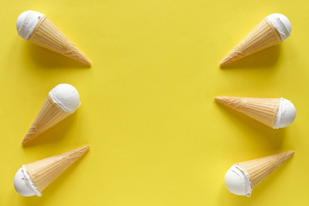 Double side border of vanilla ice cream cones on a colorful yellow background with central copy space for summer themed conceptsの写真素材